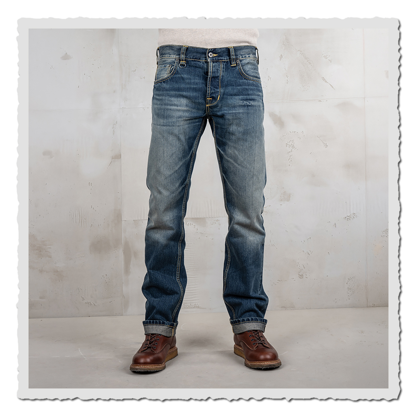 Vorderansicht einer getragenen blauen Jeans mit hellen Waschungen, umgeschlagenen Säumen und braunen Schuhen im Studio.